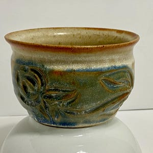 Peut inclure: Un petit bol en céramique fait à la main avec un glaçage brun clair et un motif floral vert et bleu.