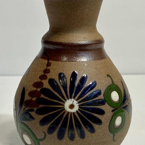 May include: A brown ceramic vase with a wide mouth and a round body. The vase is decorated with hand-painted blue, green, and red flowers and leaves.