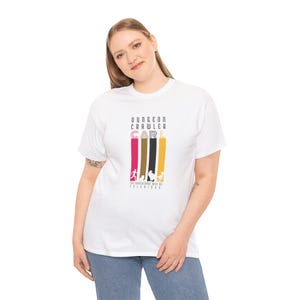 Pode incluir: T-shirt branco com o texto "DUNGEON CRAWLER CARL" num design vertical com barras coloridas e silhuetas. A frase "THE APOCALYPSE WILL BE TELEVISED" est&aacute; impressa abaixo.