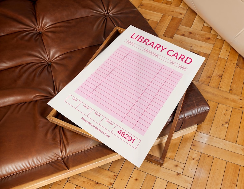 Puede incluir: Una impresi&oacute;n de tarjeta de biblioteca blanca y rosa con las palabras "LIBRARY CARD" en rosa. La impresi&oacute;n est&aacute; en una bandeja de madera sobre un sof&aacute; de cuero marr&oacute;n. La impresi&oacute;n tiene l&iacute;neas para informaci&oacute;n y el texto "Please Return Books on Time".