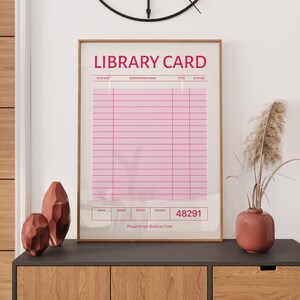 Puede incluir: Un estampado enmarcado con un dise&ntilde;o de tarjeta de biblioteca rosa. El texto "LIBRARY CARD" est&aacute; en la parte superior, con campos para detalles como la fecha de vencimiento y el nombre del prestatario. La parte inferior dice "Please Return Books on Time."