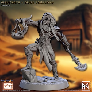 Może przedstawiać: Szara miniaturowa figurka szkieletowego faraona, trzymającego wagę i zakrzywiony miecz. Figurka stoi na skalistej podstawie. Tekst "GUL'RATH + DUNE TOMBLORD" znajduje się na górze. Podstawa ma 30 mm. Figurka jest z Artisan Guild.