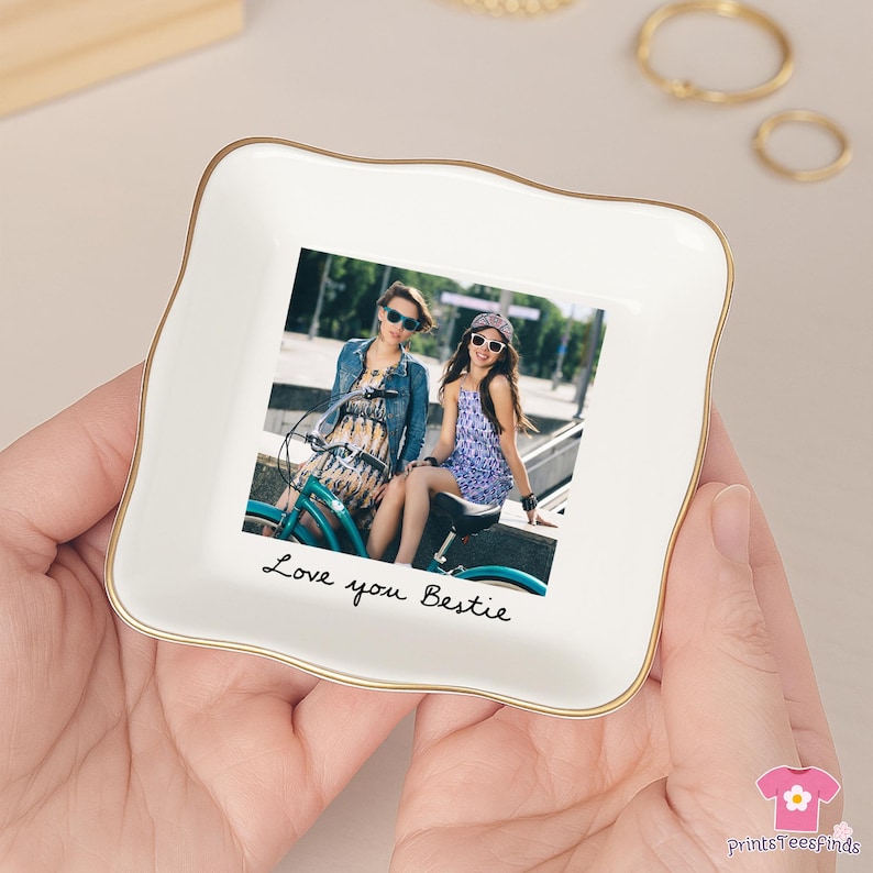 May include: A white ceramic trinket dish with a gold rim, featuring a photo of two people on a bicycle. The dish has the words "Love you Bestie" written in black script.