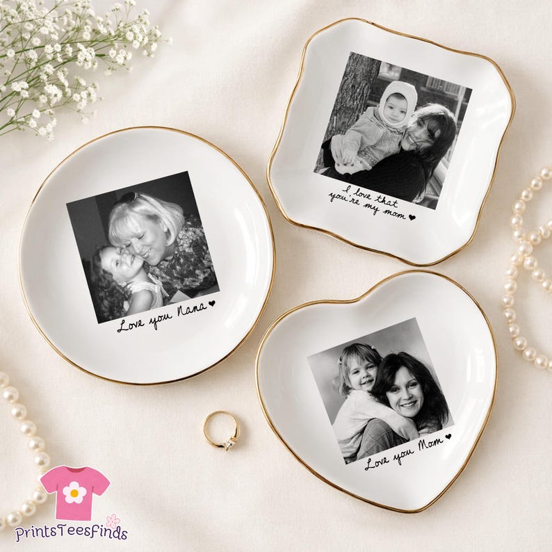 May include: Three white ceramic trinket dishes with gold rims, each featuring a black and white photograph. One is round, one is square-shaped, and one is heart-shaped. Each dish has a handwritten message: "Love you Nana", "I love that you're my mom", and "Love you Mom".