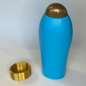 May include: A blue plastic bottle with a gold-colored cap and a separate gold-colored ring. The bottle is tall and cylindrical, and the ring is short and round. The items are on a white surface.