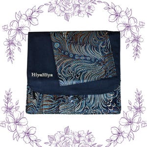 Puede incluir: Un embrague de tela azul oscuro con una solapa de patrón decorativo. La solapa presenta un diseño azul, verde y dorado. El embrague tiene el texto "HiyaHiya" bordado en la parte delantera.