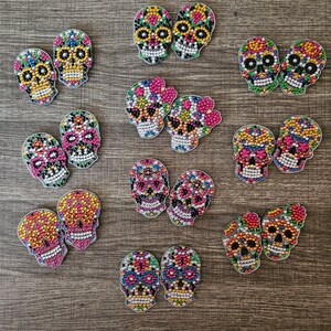 Puede incluir: Una colección de 10 pares de kits de pintura de diamantes con forma de calavera de azúcar de colores. Cada kit presenta un diseño diferente con varios colores, incluidos el rosa, el amarillo, el azul y el verde.