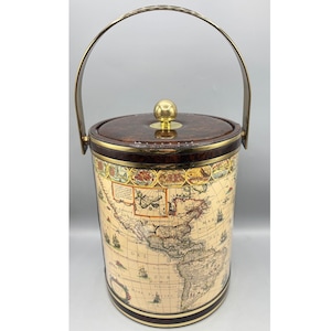 May include: Vintage ice bucket with a world map design. The cylindrical bucket features a brass handle and a lid with a gold-colored knob. The map design is printed on a cream-colored background with brown and gold accents.