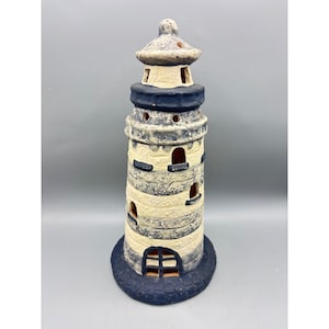 May include: A ceramic lighthouse with a blue and white striped design. The lighthouse has a dark blue base and top, with small windows and a detailed roof. The lighthouse is approximately 10 inches tall.