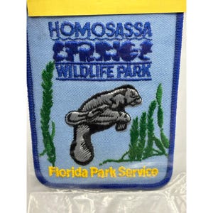 May include: A blue and yellow embroidered patch with the text "Homosassa Springs Wildlife Park" and "Florida Park Service". A gray manatee is swimming in the center of the patch.