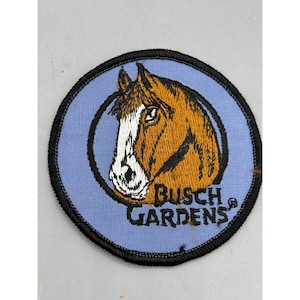 Könnte beinhalten: Ein blauer gestickter Aufnäher mit einem braunen Pferdekopf und dem Text "Busch Gardens" in Schwarz.