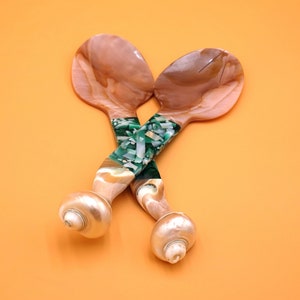 May include: A pair of iridescent mother-of-pearl salad servers with green and white marbled handles. The handles are shaped like seashells.