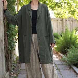 May include: A long olive green linen coat with a lapel collar and two pockets. The coat is worn over a black top and paired with beige linen trousers. The outfit is casual and comfortable, suitable for everyday wear.
