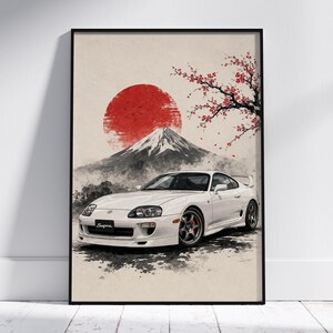 Peut inclure: Une affiche murale encadrée représentant une voiture de sport Toyota Supra blanche garée devant un mont Fuji stylisé. L'arrière-plan comprend un grand soleil rouge et une branche de cerisier en fleurs avec des fleurs rouges sur fond beige.