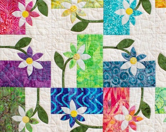 May include: A quilt with a white background and a patchwork design of colorful floral fabric squares. The quilt features a repeating pattern of white flowers with yellow centers and green stems.