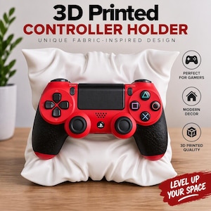 May include: A white 3D printed controller holder shaped like a plush pillow, featuring a red and black video game controller resting on its front. The text 3D PRINTED CONTROLLER HOLDER and LEVEL UP YOUR SPACE are visible on the display.