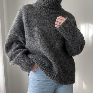 Puede incluir: Un su&eacute;ter gris de cuello alto de gran tama&ntilde;o con un corte holgado. El su&eacute;ter est&aacute; hecho de un material suave y peludo.