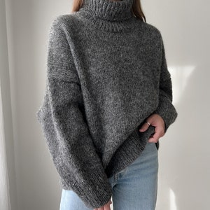 Puede incluir: Un su&eacute;ter gris de cuello alto, de corte holgado y mangas largas.