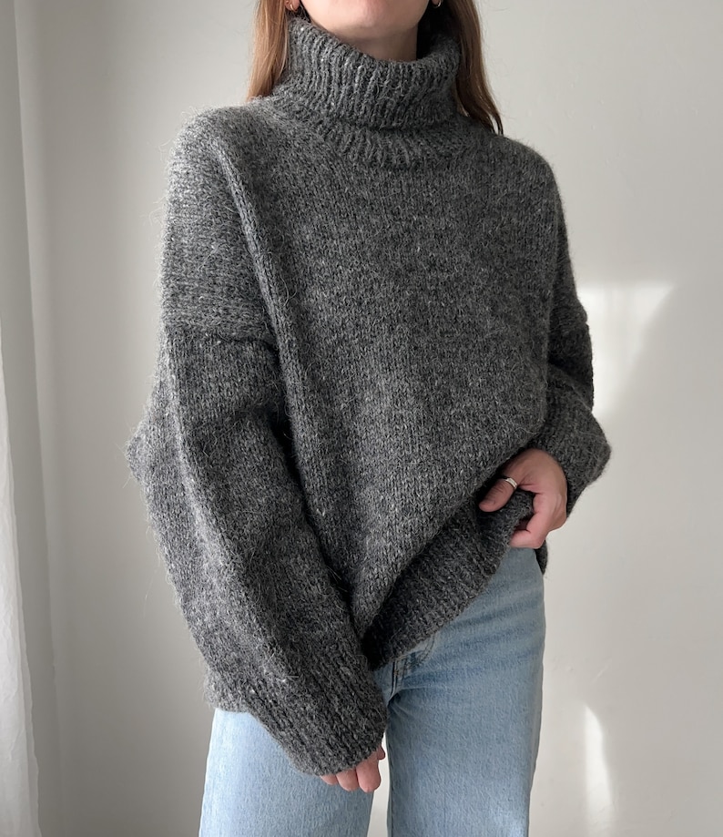 Puede incluir: Un su&eacute;ter gris de cuello alto, de corte holgado y mangas largas.