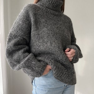 Puede incluir: Un su&eacute;ter gris de cuello alto, de corte holgado y mangas largas.