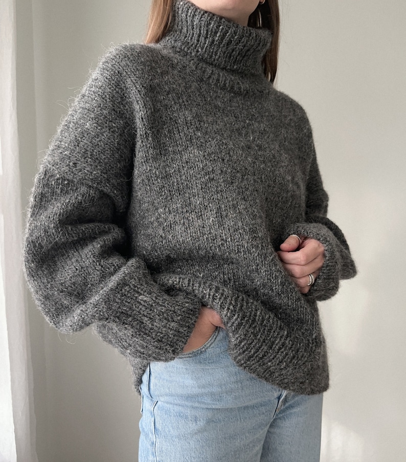 Puede incluir: Un su&eacute;ter gris de cuello alto, de corte holgado y mangas largas.