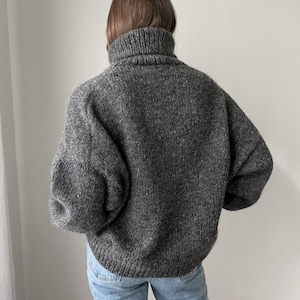 Puede incluir: Un su&eacute;ter gris de cuello alto con un corte holgado y mangas largas. El su&eacute;ter est&aacute; hecho de un material suave y peludo.