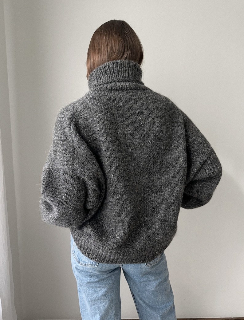 Puede incluir: Un su&eacute;ter gris de cuello alto con un corte holgado y mangas largas. El su&eacute;ter est&aacute; hecho de un material suave y peludo.