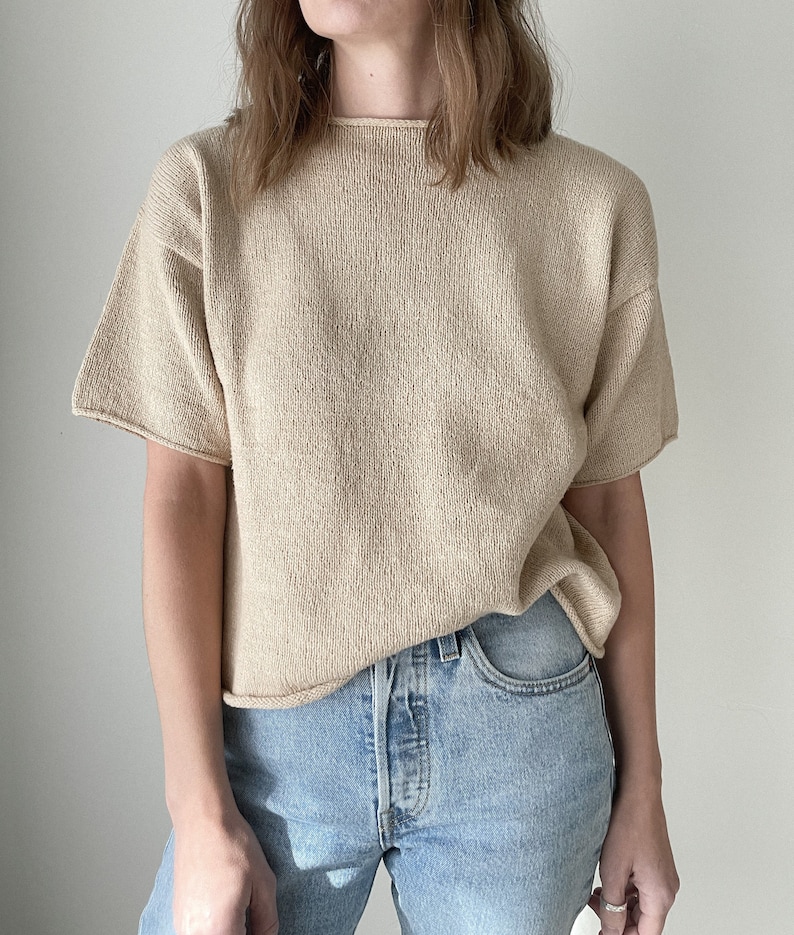May include: A beige knitted short-sleeved top with a round neckline. The top is made of a soft, lightweight fabric and has a relaxed fit.