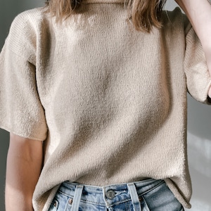 May include: A beige knitted sweater with short sleeves. The sweater is made of a soft, textured fabric and has a relaxed fit.