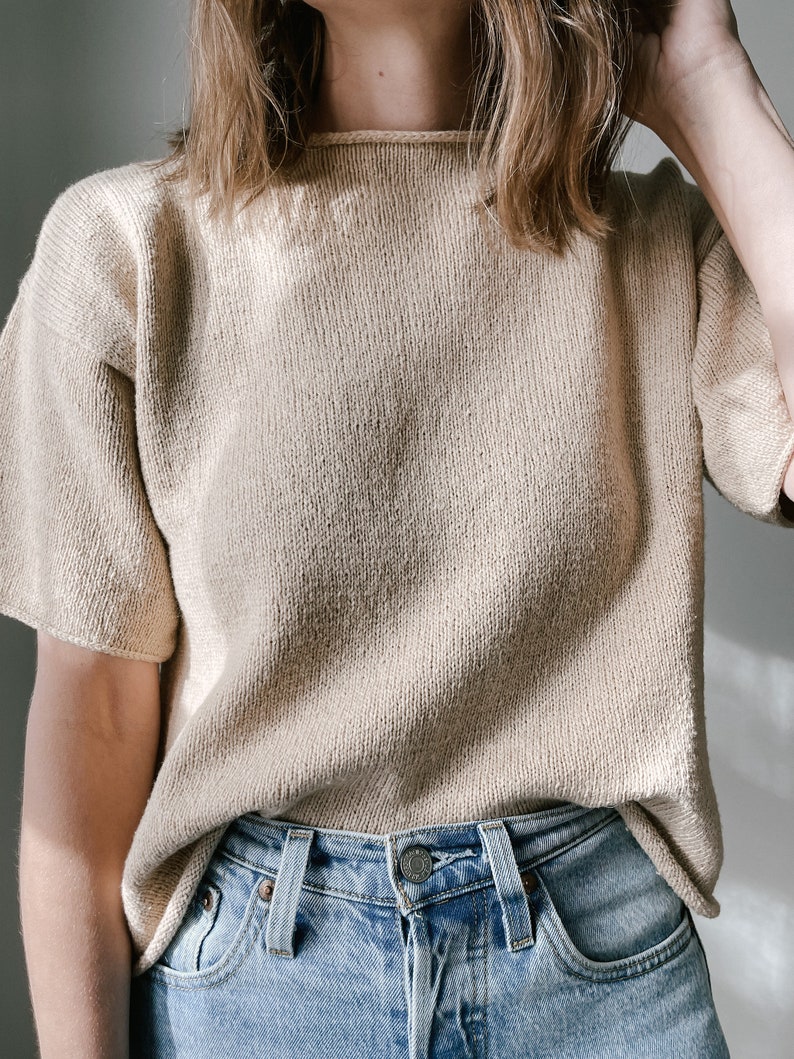 May include: A beige knitted sweater with short sleeves. The sweater is made of a soft, textured fabric and has a relaxed fit.
