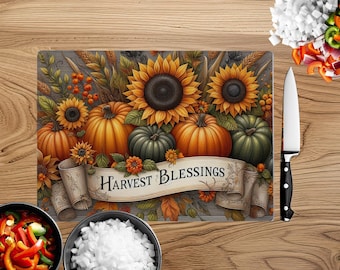 May include: A glass cutting board with a fall harvest theme. The board features a banner with the text "Harvest Blessings" and is decorated with pumpkins, sunflowers, and fall foliage.