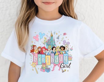 Puede incluir: Una camiseta blanca de manga corta con un estampado gráfico colorido de varias princesas animadas, un castillo, globos y cajas de regalo. El texto "birthday Girl" está impreso en el centro junto a una varita mágica y motivos festivos.