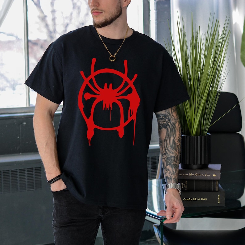 Puede incluir: Camiseta negra con un gr&aacute;fico rojo de una ara&ntilde;a en un c&iacute;rculo con pintura goteando. La ara&ntilde;a est&aacute; estilizada y tiene un contorno rojo.