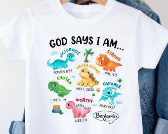 May include: White t-shirt featuring colorful dinosaur illustrations and the text "GOD SAYS I AM..." with various affirmations. The shirt includes the name "Benjamin" in a speech bubble, and Bible verses.