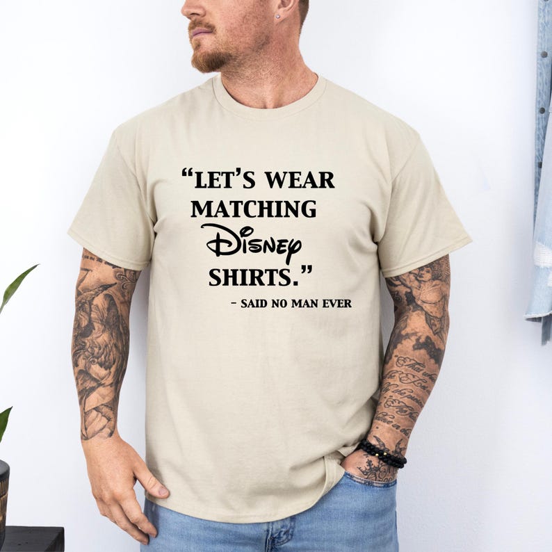 Peut inclure: T-shirt beige avec l'inscription noire "LET'S WEAR MATCHING Disney SHIRTS." et "- SAID NO MAN EVER". Le t-shirt est de style col rond et est port&eacute; par une personne.