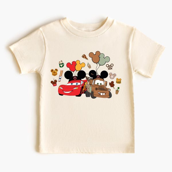 May include: Cream-coloured t-shirt featuring a graphic of Lightning McQueen and Mater from the Cars movie, each with Mickey Mouse ears. Balloons and other Disney-themed icons surround the cars. The shirt is made of a soft material.