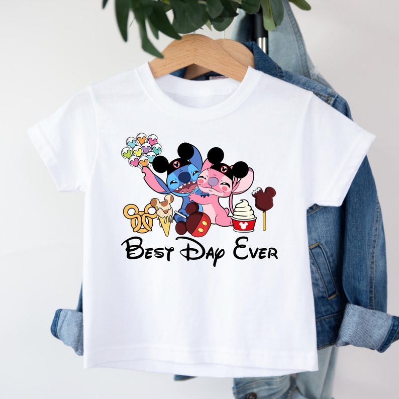 May include: White t-shirt featuring a graphic of two cartoon characters hugging, with the text "Best Day Ever." The design includes colorful treats and Mickey Mouse-themed elements.