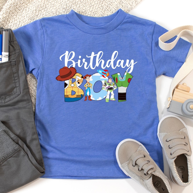 May include: Blue t-shirt with a white graphic of the characters from the Toy Story movie. The graphic says "Birthday Boy" with the characters forming the letters.