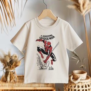 May include: A white t-shirt with a graphic print of Spiderman swinging through the city. The text "the AMAZING SPIDER-MAN" is printed above the image.