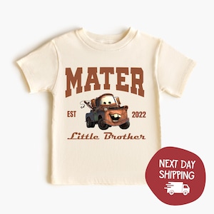May include: Cream-colored t-shirt featuring the word "MATER" in brown block letters above a cartoon image of Mater from the Cars movie. Below the image, the text reads "Little Brother" and "EST 2022".