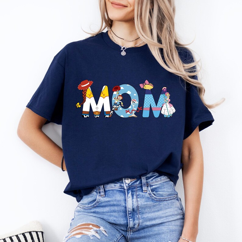 K&ouml;nnte beinhalten: Ein marineblaues T-Shirt mit einem Aufdruck der Toy Story-Charaktere, die das Wort "MOM" buchstabieren.