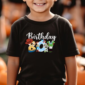 May include: A black t-shirt with a white graphic of Toy Story characters spelling out "Birthday Boy".