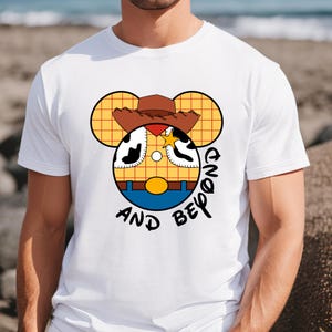 May include: White t-shirt with a cartoon image of Woody from Toy Story in a Mickey Mouse silhouette. The text "And Beyond" is written below the image.
