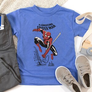 May include: A blue t-shirt with a graphic of Spider-Man swinging through the city. The text "the AMAZING SPIDER-MAN" is printed on the shirt.