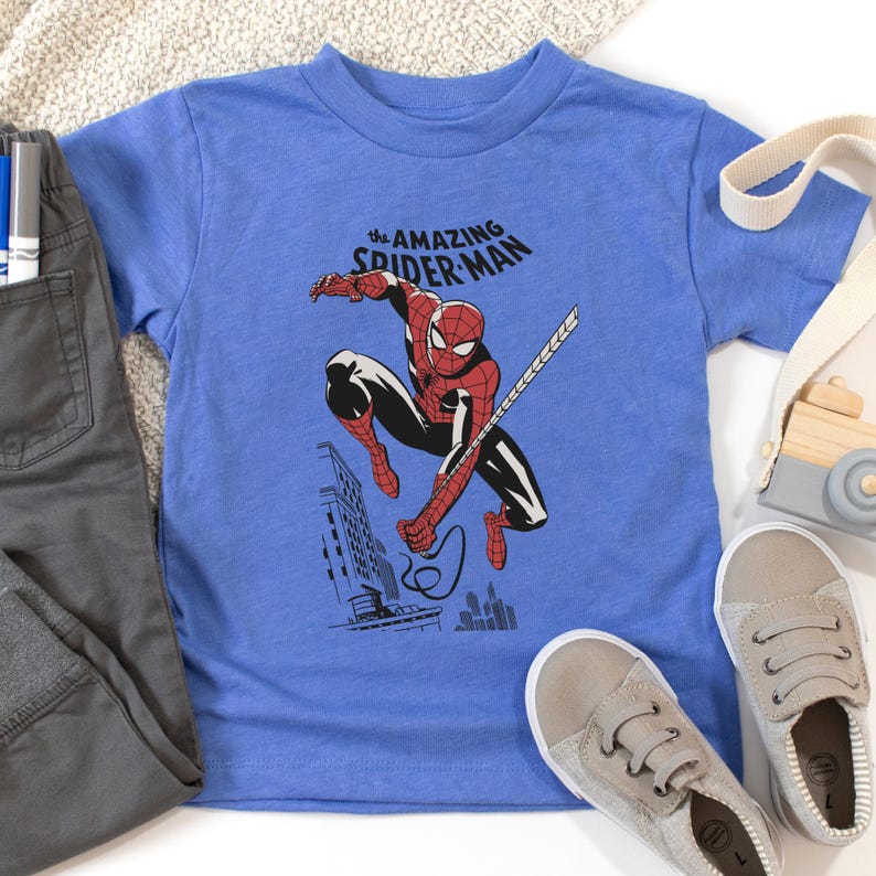 May include: A blue t-shirt with a graphic of Spider-Man swinging through the city. The text "the AMAZING SPIDER-MAN" is printed on the shirt.