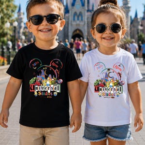 May include: A black t-shirt and a white t-shirt, each featuring a colorful graphic print with the text Universal Studios, 2026, and a placeholder for a name. The design includes various cartoon characters, a castle silhouette, and a crescent moon.