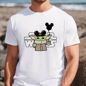 May include: White t-shirt featuring a green cartoon character wearing a Mickey Mouse hat and holding a black balloon. The text "STAR WARS" is printed on the shirt.
