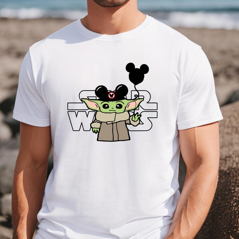 May include: White t-shirt featuring a green cartoon character wearing a Mickey Mouse hat and holding a black balloon. The text "STAR WARS" is printed on the shirt.