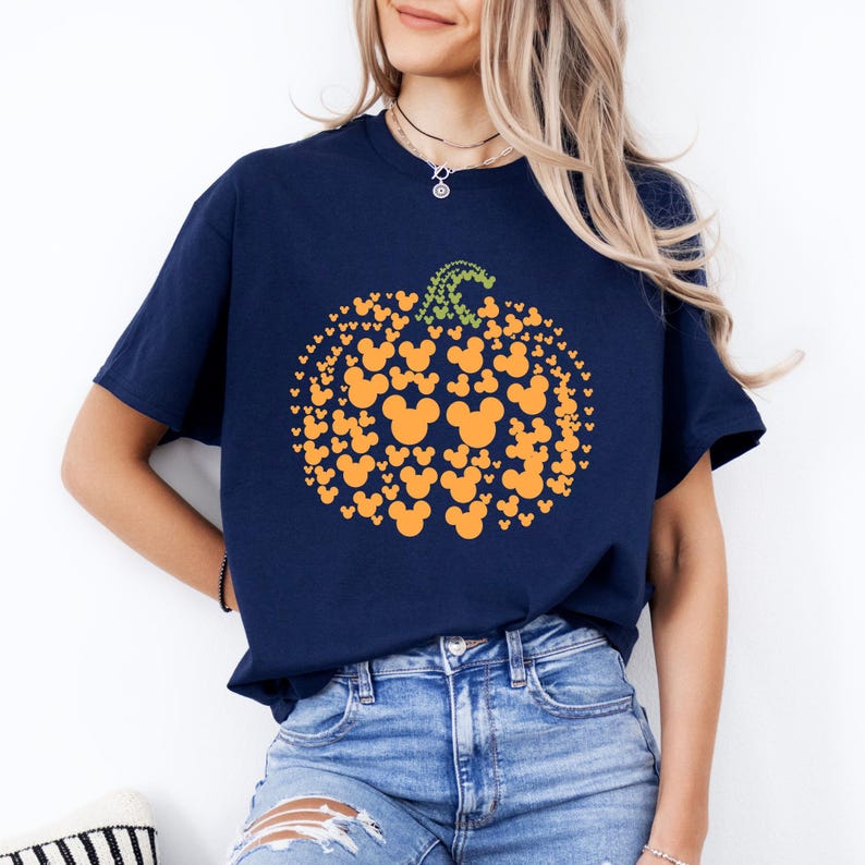 Puede incluir: Camiseta azul marino con un dise&ntilde;o de calabaza hecho de siluetas naranjas de Mickey Mouse y un tallo verde. La camiseta es de cuello redondo y manga corta.