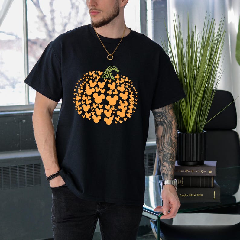 Puede incluir: Camiseta negra con un dise&ntilde;o de calabaza hecho de siluetas naranjas de Mickey Mouse y un tallo verde. La camiseta es de cuello redondo y manga corta.